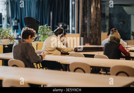 Students studying in a modern shared classroom space with headphones and notebooks Stock Photo