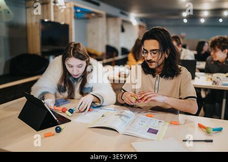 Two students collaborating on a study project with tablet and textbooks in a modern classroom Stock Photo