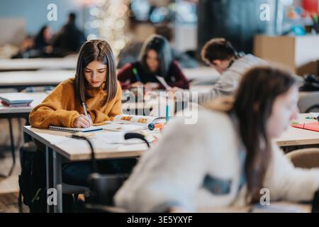 College students studying together in a bright communal classroom focusing on a young woman taking notes Stock Photo