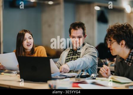 Three students studying together around a laptop in a collaborative classroom setting Stock Photo