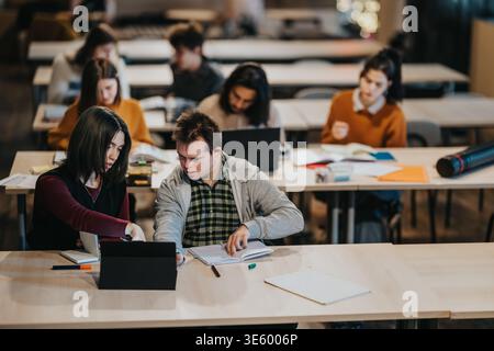 Tutor helps student with a disability using a tablet in an inclusive classroom with other students Stock Photo