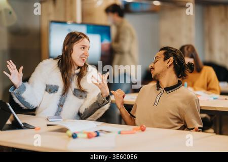 Two students having an animated discussion during a collaborative study session in a modern workspace Stock Photo