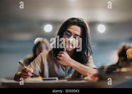 Young student with long hair and glasses studying and taking notes at a classroom desk Stock Photo