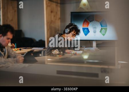 Young student studying with headphones at a coworking desk during a business presentation Stock Photo