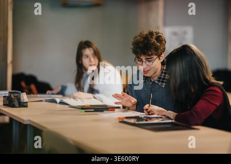 Three students studying and discussing ideas together at a table in a classroom Stock Photo