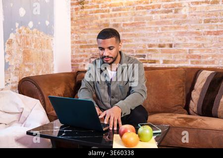 Focused young man working from home sitting on couch using laptop Stock Photo