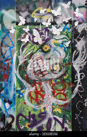 A grotesque face drawn with pastel crayons by Alex Arnell, surrounded by graffiti artwork and paper butterflies in Leonard Lane, Bristol, England, UK. Stock Photo