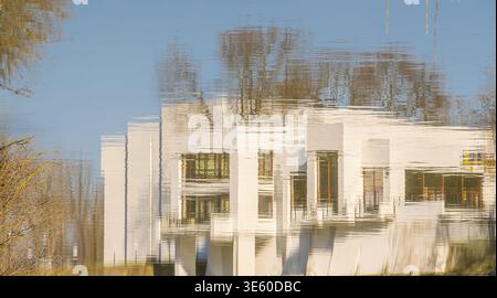 Reflection of a modern white building in calm water with ripple distortion, creating abstract architectural patterns, suitable for design backgrounds Stock Photo