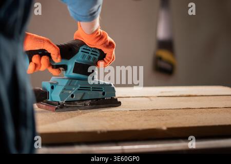 Close-up of carpenter hands with sander at workshop for polish. wood worker using electric sanding machine with plank making restoration Stock Photo