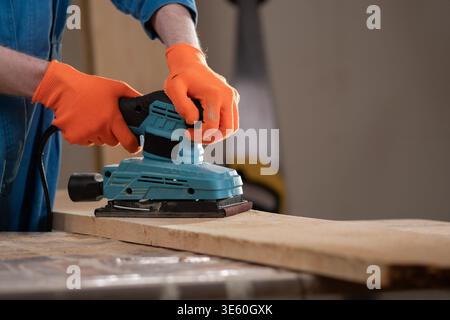 Close up carpenter hands using electric sander machine over wood. Woodworking and construction concept. Stock Photo