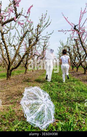 Escape from tradition, two women running in blooming orchard Stock Photo