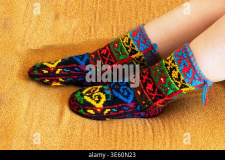 Beautiful wool socks made of multicolored threads on the girl's feet. Stock Photo