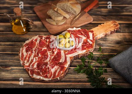 Guitar-shaped board with Serrano ham with bread, olive oil and olives Stock Photo