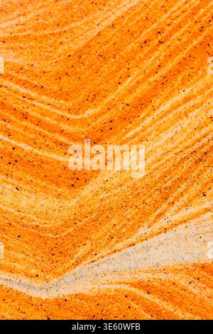 Close up yellow and orange sand forming vibrant, wavy patterns with dark mineral grains. Artistic sand art texture Stock Photo