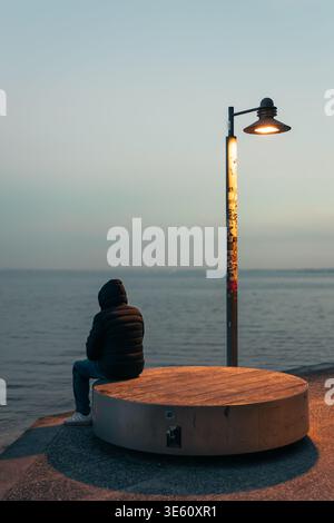 Person sitting by lake at sunset under street lamp in Italy Stock Photo