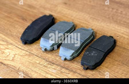 A close-up image shows a set of car brake pads placed side by side on a wooden surface, highlighting the contrast between new and worn friction materi Stock Photo