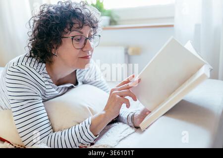 Close up female reading book while lying on bed at home Stock Photo
