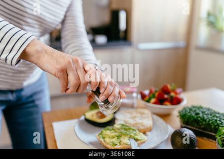 Middle aged woman seasoning avocado toast healthy breakfast diet routine clean eating Stock Photo