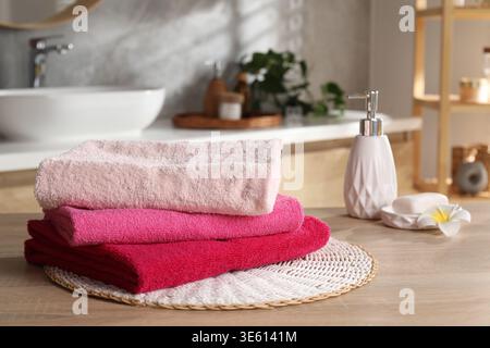 Stack of colorful towels, soap and plumeria flower on wooden table in bathroom, closeup Stock Photo