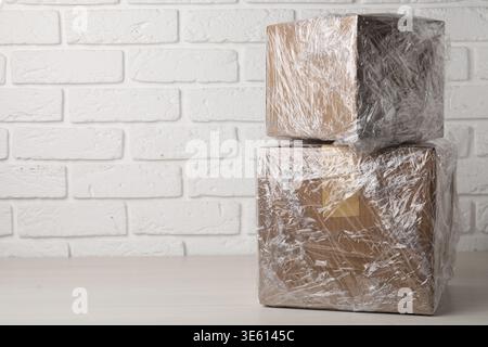 Cardboard boxes in plastic wrap on white wooden table, closeup. Space for text Stock Photo