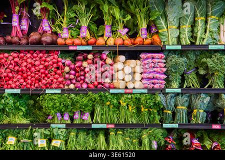 Fresh organic vegetables on supermarket shelves. Variety of radishes, beets, carrots, and leafy greens. Concept of healthy food and grocery shopping. Stock Photo