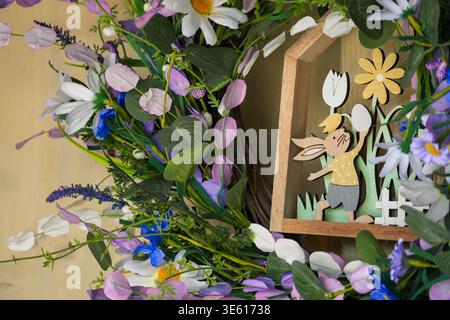 Close-up of an Easter flower wreath on a yellow wooden wall, decorated with artificial flowers and small wooden frame Stock Photo