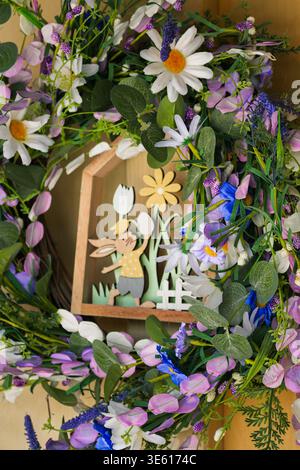 Close-up of an Easter flower wreath on a yellow wooden wall, decorated with artificial flowers and small wooden frame Stock Photo
