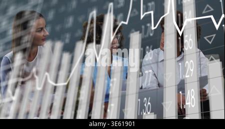 Analyzing team discussing financial data at table with laptop, wearing blue blouse and white shirt Stock Photo