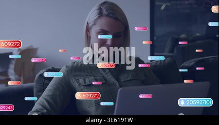 Working woman in olive-green button-up shirt typing on laptop in dim living room, with AR tags Stock Photo