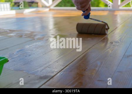 Close-up of wooden deck varnishing with roller in sunlight Stock Photo