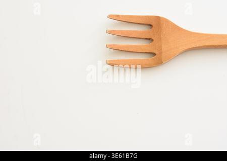 Single wooden fork placed on a white surface, highlighting natural texture and minimalist design. Perfect for concepts of eco-friendly lifestyle Stock Photo