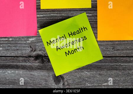 Four coloured sticky notes in the colours green, yellow, orange and pink on wooden styled surface. Green note says mental health awareness month Stock Photo
