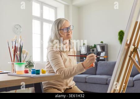 Creative elderly woman painting picture with watercolors, trying to make masterpiece Stock Photo