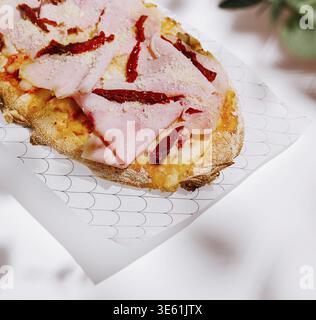 Food, A freshly baked flatbread is topped with slices of ham and sun-dried tomatoes, served on a decorative plate. The setting highlights the vibrant Stock Photo