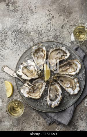 Food, Opened fresh raw oysters on gray plate served with lemon and white wine, top view, concrete background Stock Photo