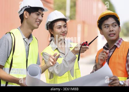 Three construction professionals, an engineer, a project manager, and a worker, collaborating on project plans with blueprints at a busy construction Stock Photo