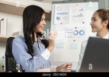 Two female professionals engage in a lively discussion, analyzing business data and strategies in a modern office environment Stock Photo