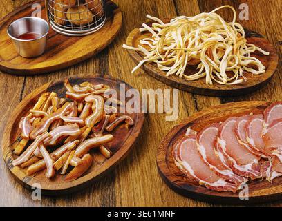 Food, A variety of cured meats and snacks are arranged on wooden platters. Included are crispy snacks, thinly sliced meats, and a small bowl of dippin Stock Photo