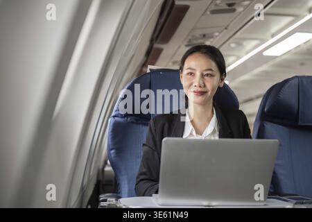 Businesswoman using a laptop on a plane, combining work and travel seamlessly Stock Photo
