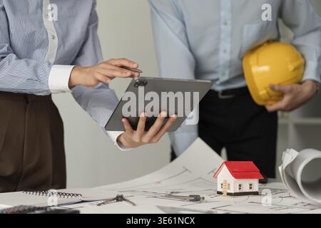 Two construction professionals engage in a collaborative discussion at their workspace, utilizing digital tools to enhance project workflows and ensur Stock Photo