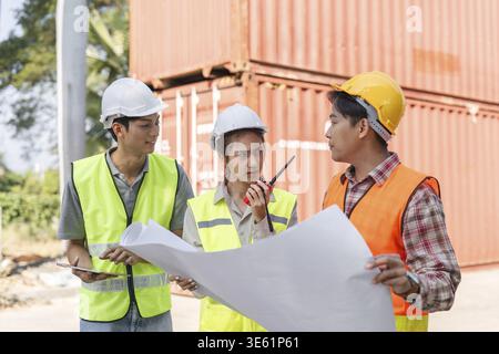 A diverse group of construction professionals, including a female supervisor and two male workers, engages in strategic discussion using blueprints an Stock Photo