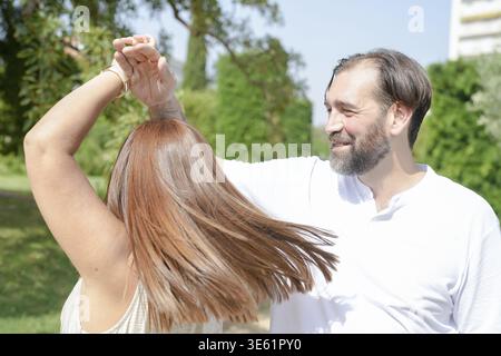 A man and a woman are dancing together in a park. The man is smiling and the woman is laughing Stock Photo
