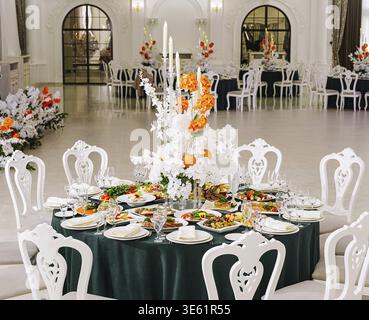 Food, A beautifully arranged banquet table showcases a variety of gourmet dishes surrounded by vibrant floral decorations. The venue is sophisticated Stock Photo