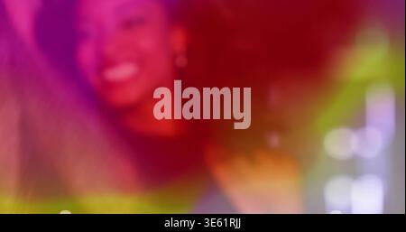 Smiling adult woman dancing at club, showing curly hair, dark top, small earring, colored lights Stock Photo