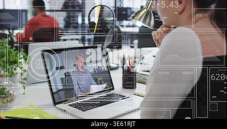 Leaning onsite worker in gray sweater watching laptop call at open office with UI overlays Stock Photo