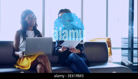 Collaborating colleagues in office on gray sofa wearing yellow skirt with laptop, blue fingerprint Stock Photo