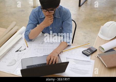 A focused architect and engineer using a laptop to work on blueprints. Concentrated on design and planning, they are engaged in creating precise and d Stock Photo