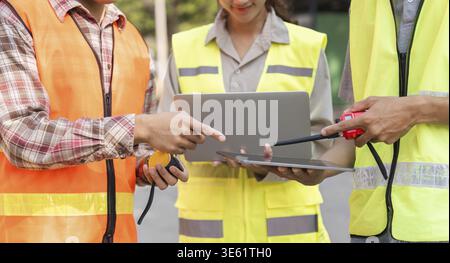 A logistics engineering team reviewing project metrics on a tablet, collaborating on data analysis at a construction site for informed decision-making Stock Photo