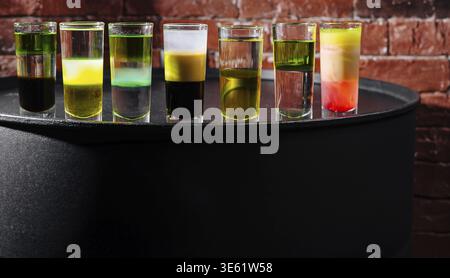 Food, Brightly colored shot glasses filled with various layered drinks line a black round table against a rustic red brick wall in a lively bar atmosp Stock Photo