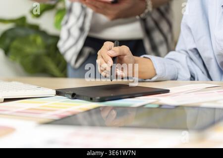 Two designers engage in a collaborative UX and UI design session, utilizing a tablet and color palettes to enhance their project Stock Photo